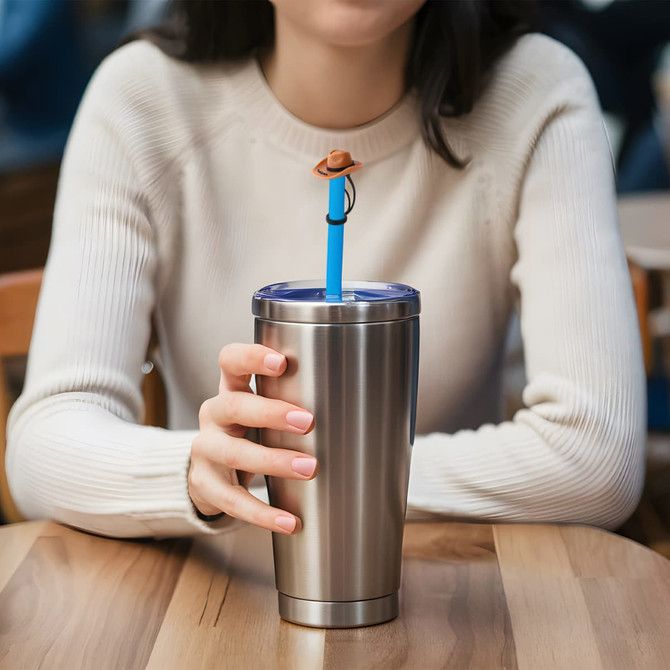 A drink bottle with a silver finish features a blue straw topped with a brown brim hat, held by a person in a light jumper.