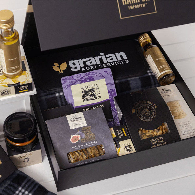 A gourmet picnic gift pack filled with olive oil, crackers, nuts, honey, and a branded box in black and white.