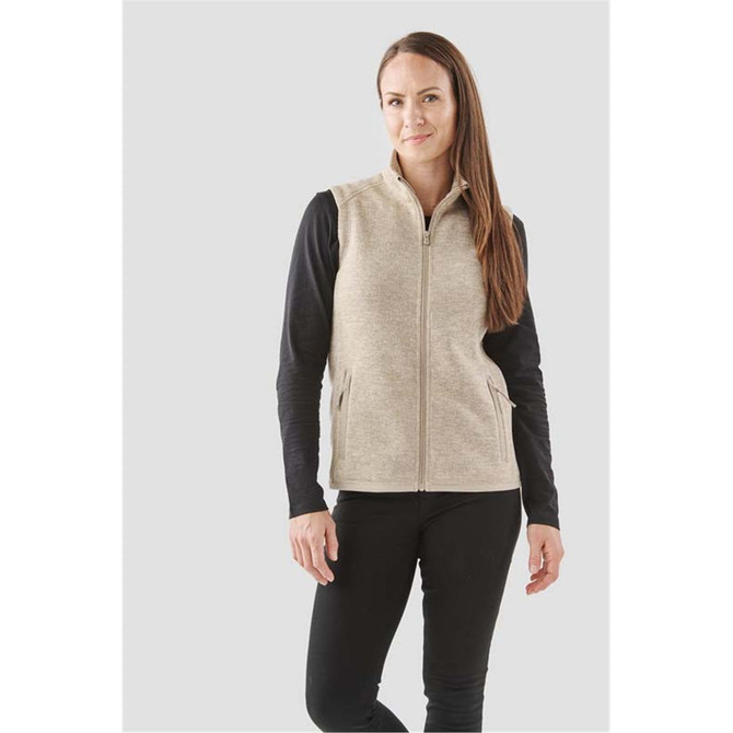 A woman models a beige full zip fleece vest, paired with a black long-sleeve top, standing against a light background.