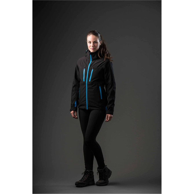 A woman wearing a black jacket with blue accents, paired with leggings and boots, standing against a dark background.