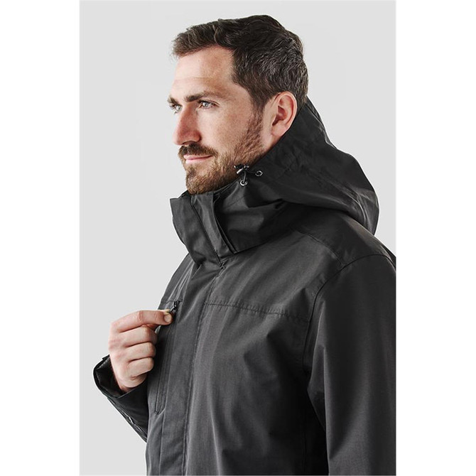 A man wearing a black Magellan System jacket, featuring a hood and front zipper, with a logo visible.