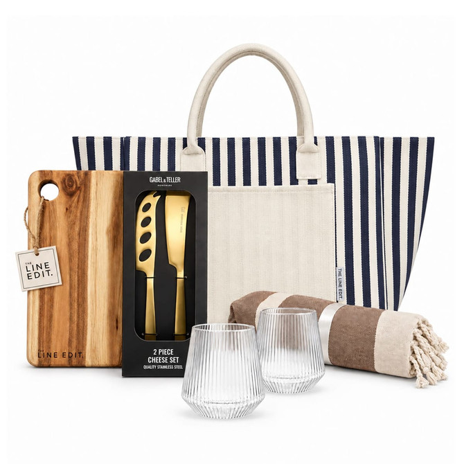 A striped tote bag contains a cheese set, a wooden cutting board, two glass tumblers, and a striped blanket.
