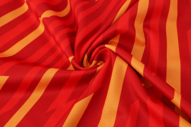 A close-up of a red fabric featuring bold yellow and orange striped patterns, displaying a smooth micro mesh texture.