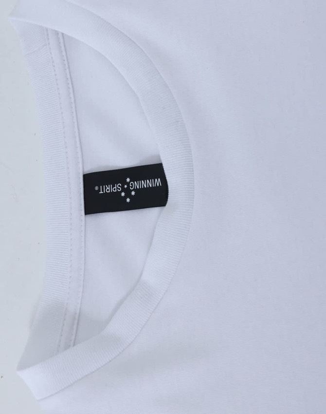A white long sleeve tee shirt with a rounded neckline and a tag displaying branding.
