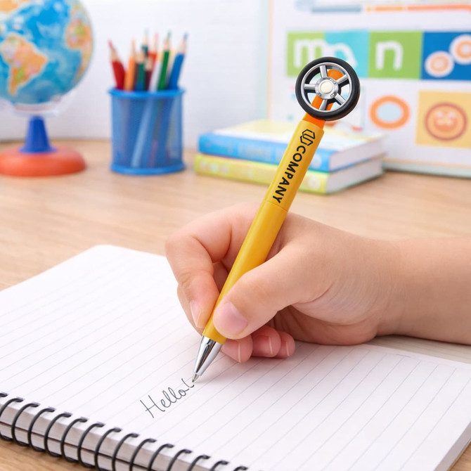 A yellow pen shaped like a tyre, featuring a fidget spinner design, resting on a notepad with handwritten text.