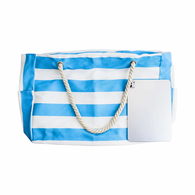 A blue and white striped beach bag with rope handles and a silver tablet placed beside it. It features a logo.