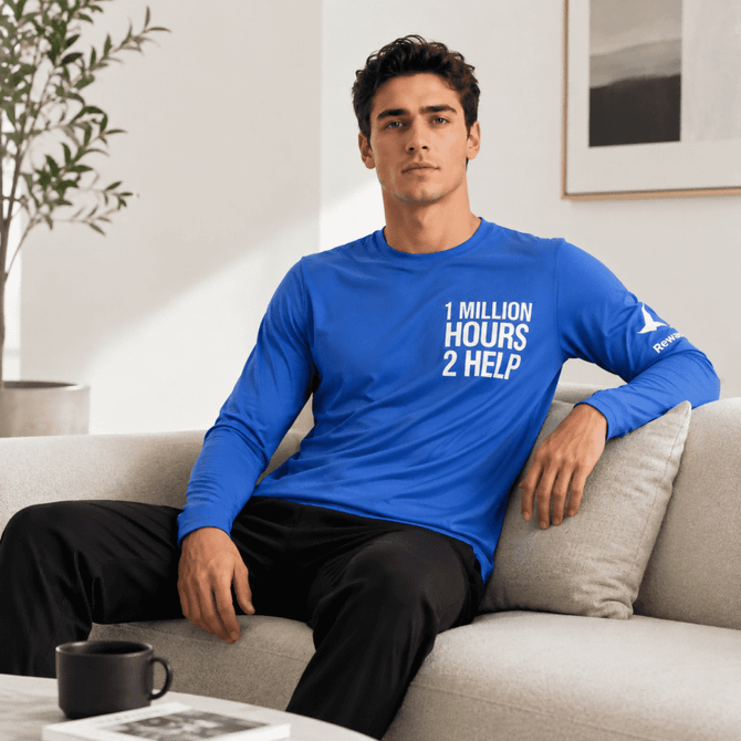 A blue unisex long-sleeve crew neck shirt with a logo, displayed on a model sitting on a sofa.