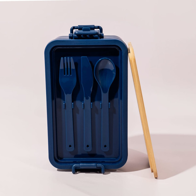A navy blue lunch box with a bamboo lid, featuring a fork, knife, and spoon inside. The box has a logo.