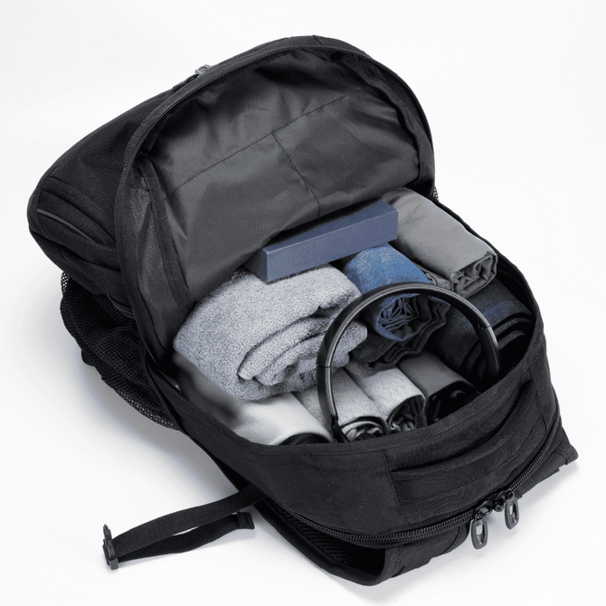A black backpack with neatly arranged rolled clothes, a box, and a pair of headphones inside.