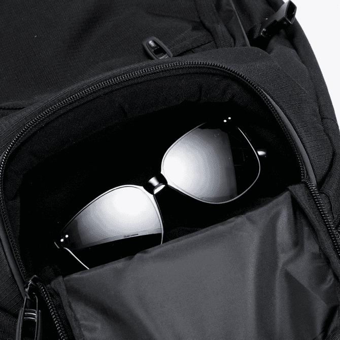 A black backpack with a zippered pocket containing a pair of dark sunglasses inside.