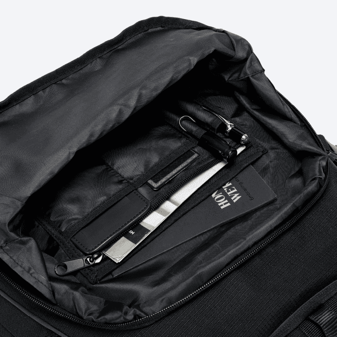 An open black backpack interior featuring a pen, a cardholder, and a small notebook.