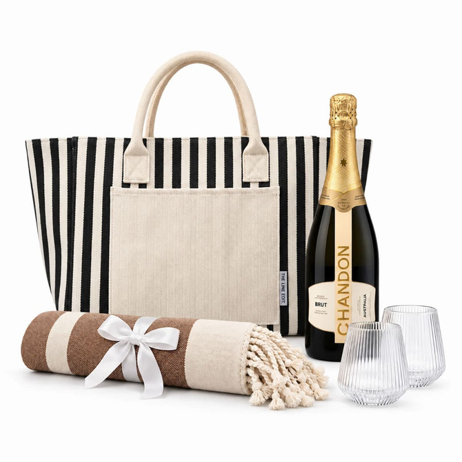 A striped tote bag, a bottle of sparkling wine, two glasses, and a rolled blanket with a ribbon.