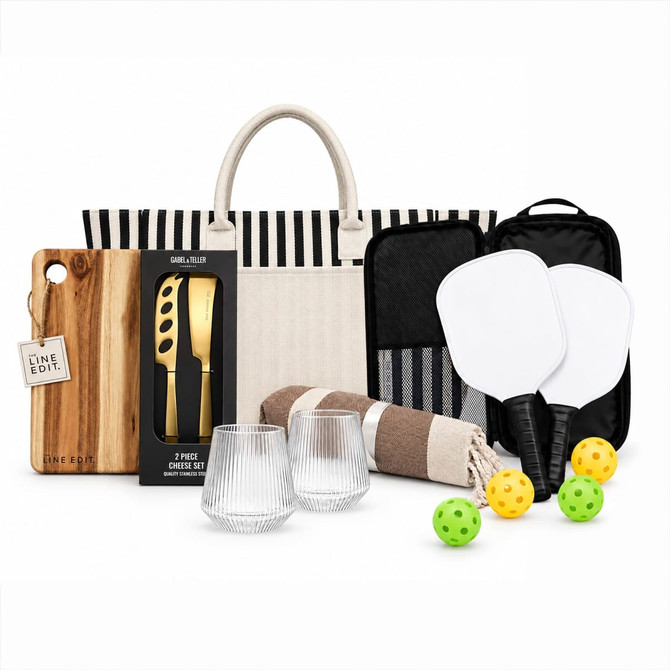A picnic set featuring a striped tote, glasses, a wooden board, utensils, a blanket, and paddle games with balls.