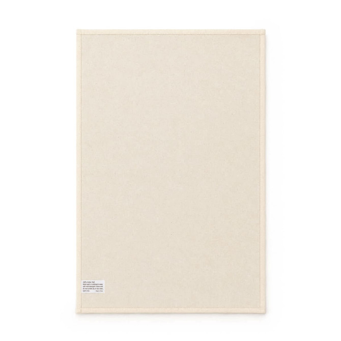 A medium cotton tea towel in a cream colour, featuring a small tag and a simple, plain design.