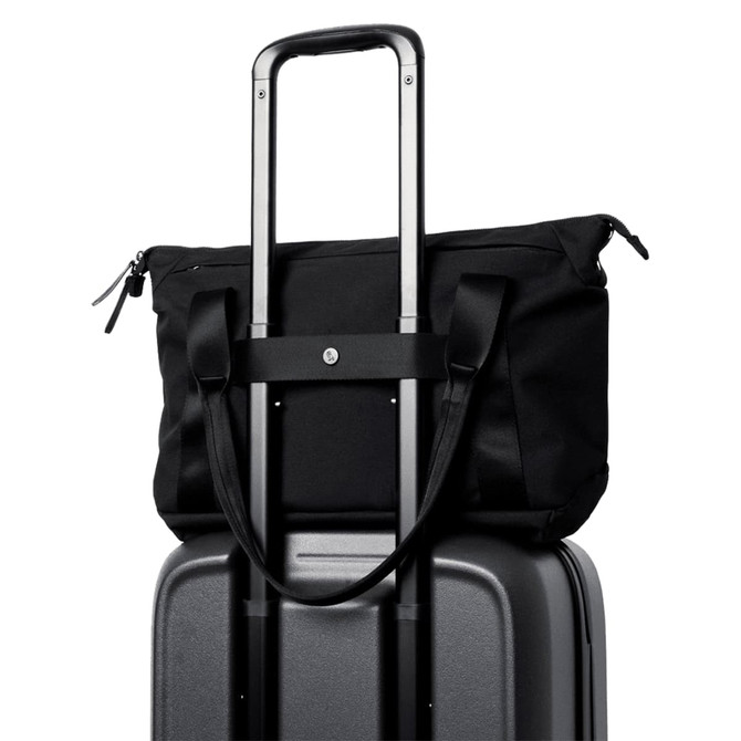 A black tote bag perched on top of a grey suitcase, featuring handles and a strap for carrying.