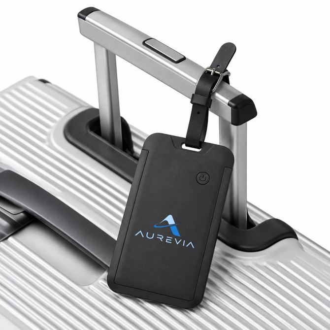 A black luggage tag tracker attached to the handle of a silver suitcase, featuring a logo.