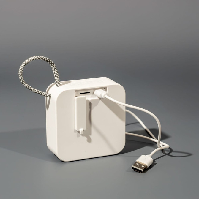 A white portable Bluetooth speaker with a flexible cord and USB connection. It has a simple, modern design.