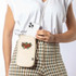 A cream-coloured bag with floral embroidery, worn crossbody, with a phone partially visible inside.