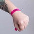 A pink wristband with a logo, worn on a wrist adorned with a tattoo.