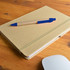 A natural-colored notebook with an elastic band lies on a wooden surface, accompanied by a blue and kraft pen.