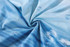 A blue sublimated polyester spandex fabric with a textured pattern, featuring cloud-like designs.