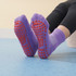 Purple gripper socks with red non-slip soles, designed for kids, displayed on a blue floor.