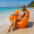 An inflatable chair in bright orange sits on the beach, with a woman in a white bikini lounging comfortably.