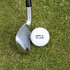 A golf ball in white positioned next to a golf club on green grass, featuring a logo on the ball.