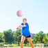 A volleyball is flying through the air as a woman in a blue shirt prepares to hit it outdoors.