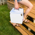 A metal cooler box in white being carried up wooden steps, featuring a handle and silver accents.