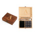 A wooden box featuring a logo, containing nine black whiskey stones and two stirring utensils.