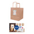 A kraft paper bag with flat handles, featuring a decorative label and a logo. The bag is a natural brown colour.