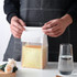 A clear bag with a white top seal containing a loaf of bread, positioned next to a glass of water.