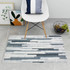 A soft flannel logo mat featuring a pattern of grey and white stripes, placed on a tiled floor with a chair and decor.