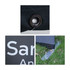 Close-up of a black Sidewalk Cafe Barrier featuring a grommet, a logo, and a base anchor on grass.