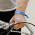 A blue wristband worn on a wrist, featuring a logo, secured to a hand holding bicycle handlebars.
