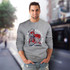 A grey unisex sweatshirt featuring a graphic of colourful sneakers. The model is smiling while wearing it.