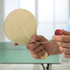A wooden paddle with a red ball attached by white string, held in a hand against a blurred background.