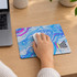 A colourful mouse mat with a blue and purple marbled design, featuring a logo in the bottom corner and a mouse on top.