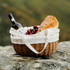 A wicker tote bag filled with a bottle of wine, grapes, and a loaf of bread, featuring white fabric lining.