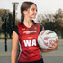 A woman in a red and black netball bib holds a netball, with a sports court in the background.