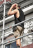 A sleeveless black tee worn by a man on scaffolding, paired with khaki shorts and work boots, during a construction task.