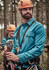 A blue long sleeve button-up shirt worn by a man, in a forest setting, with climbing gear and a helmet.
