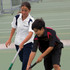 A white polo shirt with navy accents and a dark polo shirt with red accents, worn by two young athletes on a tennis court.