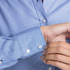 A close-up of a blue and white check patterned button-up shirt, featuring a cuff with buttons and a logo.