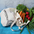A cotton shopping tote in cream with a mesh top, filled with carrots, radishes, and fresh herbs.