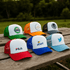 A variety of trucker caps in green, orange, white, grey, and blue, featuring multiple logos and branding.