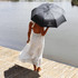 A black umbrella with a logo, held by a person in a white dress near a water body.