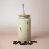 A drink bottle with a bamboo lid and stainless steel straw, filled with a creamy iced beverage and surrounded by coffee beans.