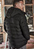 A black unisex hooded puffer jacket with a quilted design, worn by a person from a side angle.
